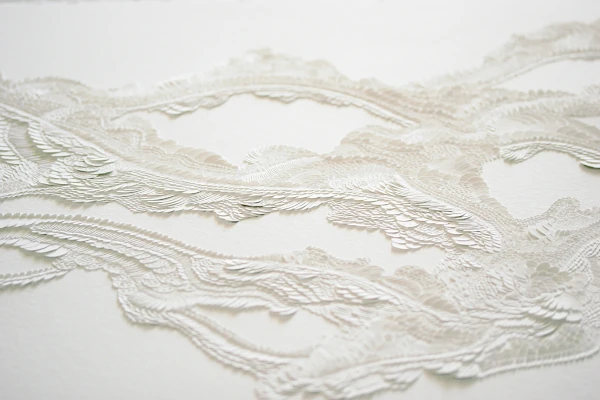 Accueil Gros plan d'un bas-relief papier incisé monochrome blanc, soulignant la texture des écailles soulevées et le jeu minimaliste d'ombre et lumière sur la surface sculptée.